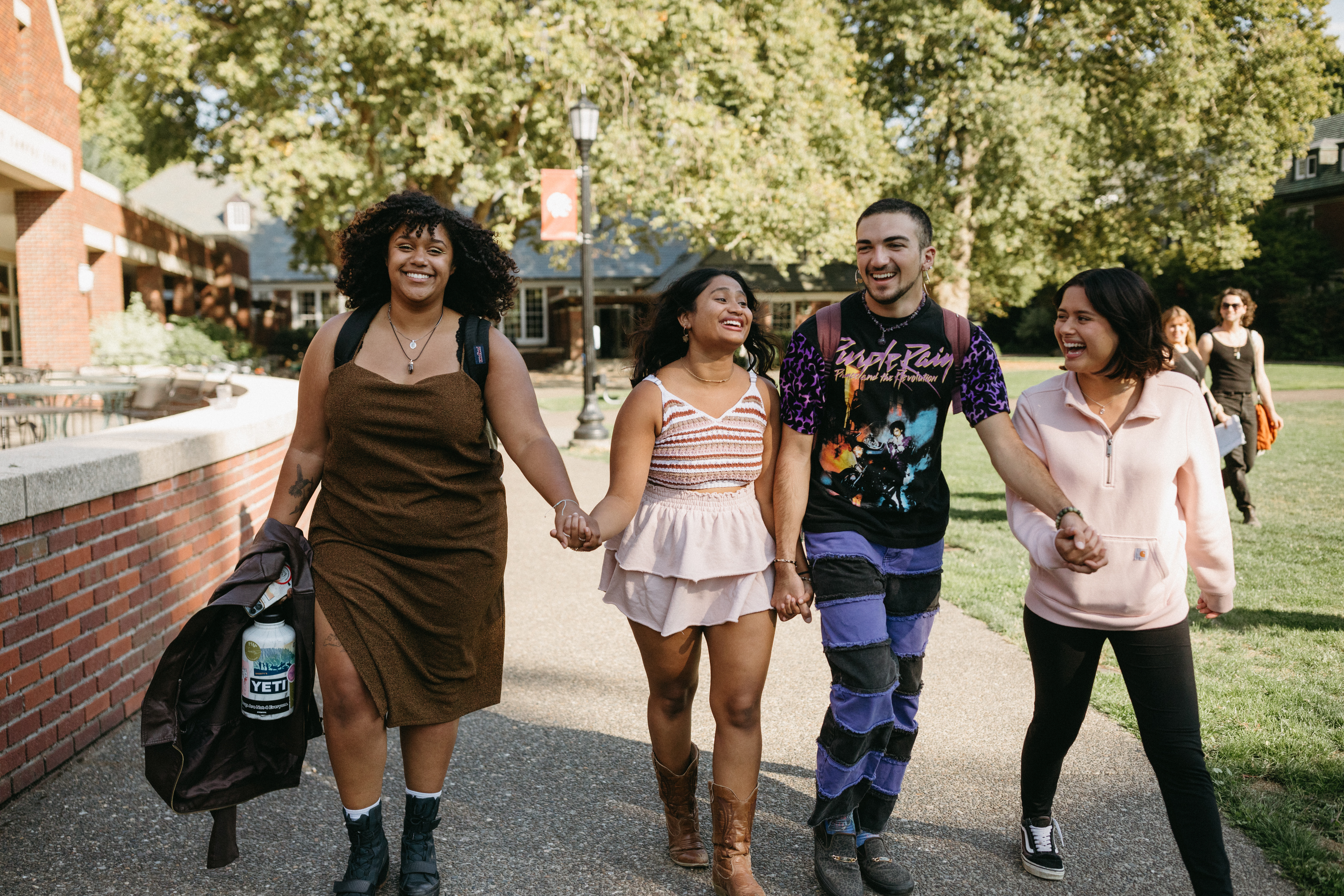 Four students holding hands while walking across campus.