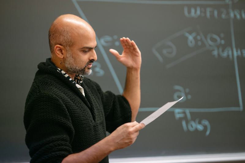 Professor reading a paper in front of a blackboard