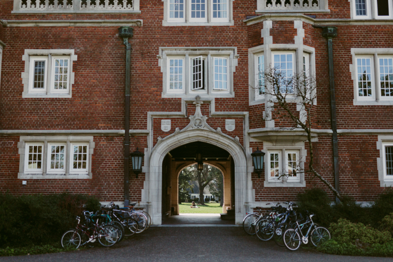 Bikes parked in front of a building at Reed, with a student sitting on the other side of the building