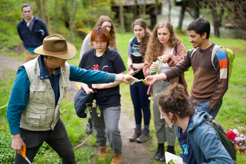 Instructor handing a student vegetation on a group walk outside campus