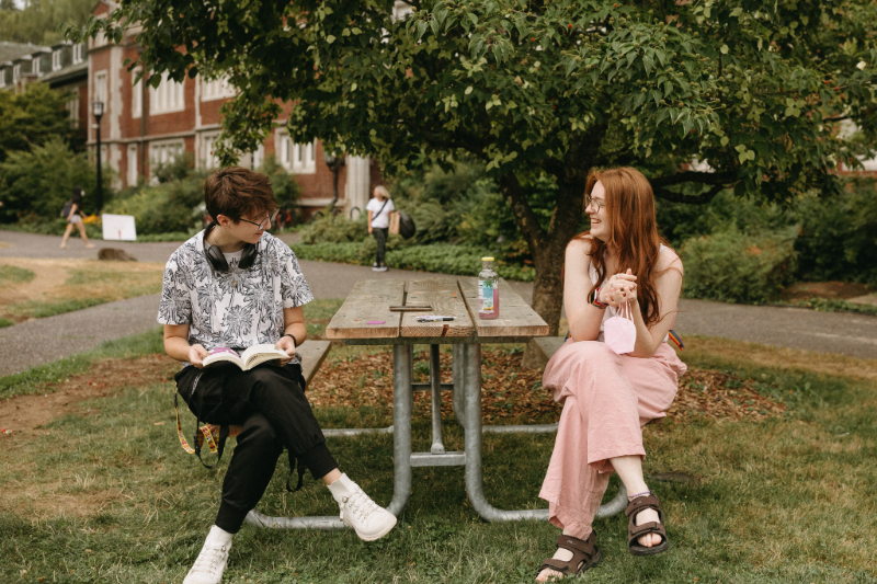 Two students sitting down at a table outside at Reed and smiling at each other