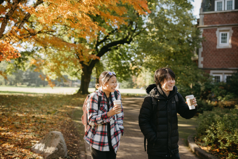 Two smiling students with cups of coffee walking down a path at Reed