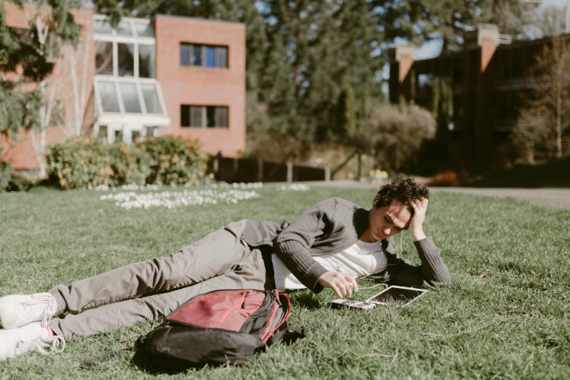 Student laying down on the grass and looking at a tablet