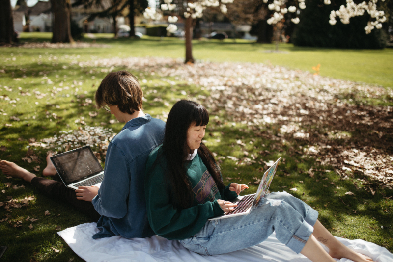 Two students with laptops sitting on grass
