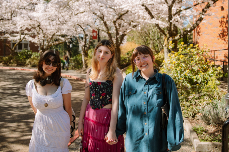 Three students standing outside at Reed with cherry blossoms blooming in the background
