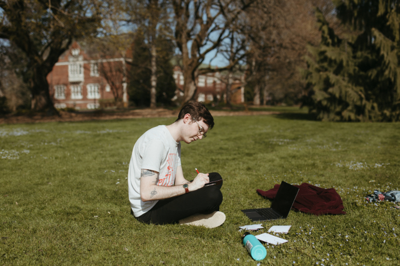 Student studying outside, sitting down on the grass at Reed