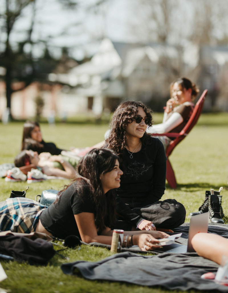 Group of smiling students sitting and laying down on the grass outside at Reed on a sunny day